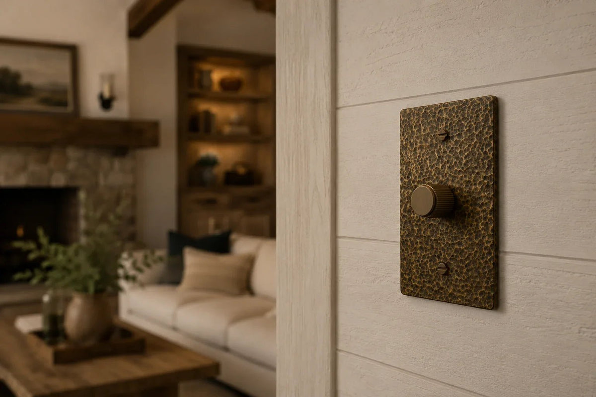 Luxury hammered brass dimmer switch installed on a white shiplap wall in a modern farmhouse living room with warm ambient lighting, rustic wood accents, and cozy neutral interior decor.