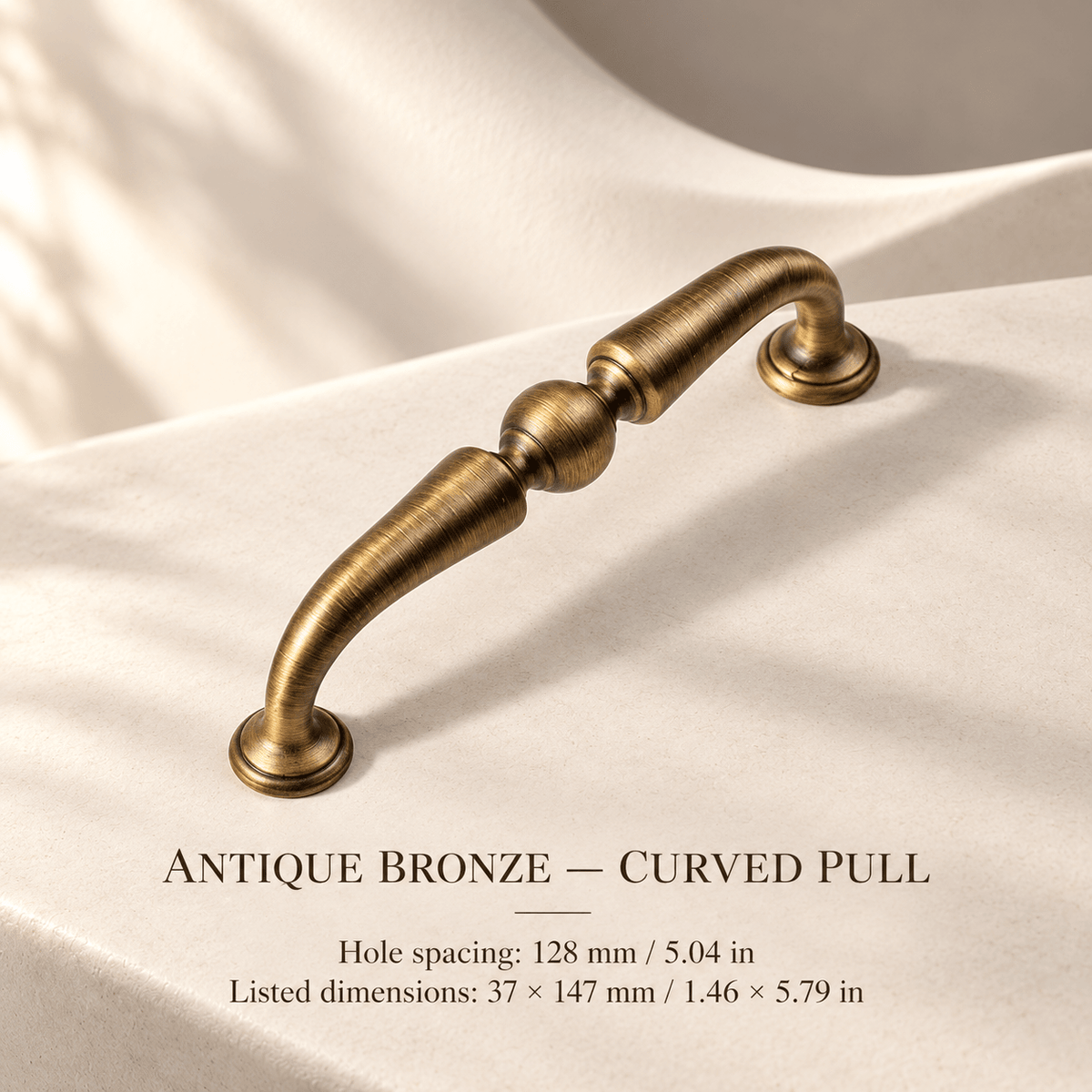 Antique bronze curved cabinet pull in ivory studio. Hole spacing: 128 mm / 5.04 in; Listed dimensions: 37 × 147 mm / 1.46 × 5.79 in