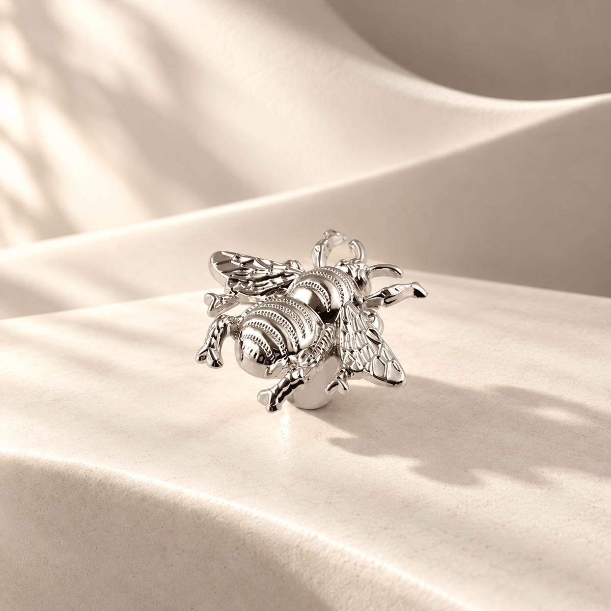 Chrome bee-shaped cabinet knob on warm ivory stone
