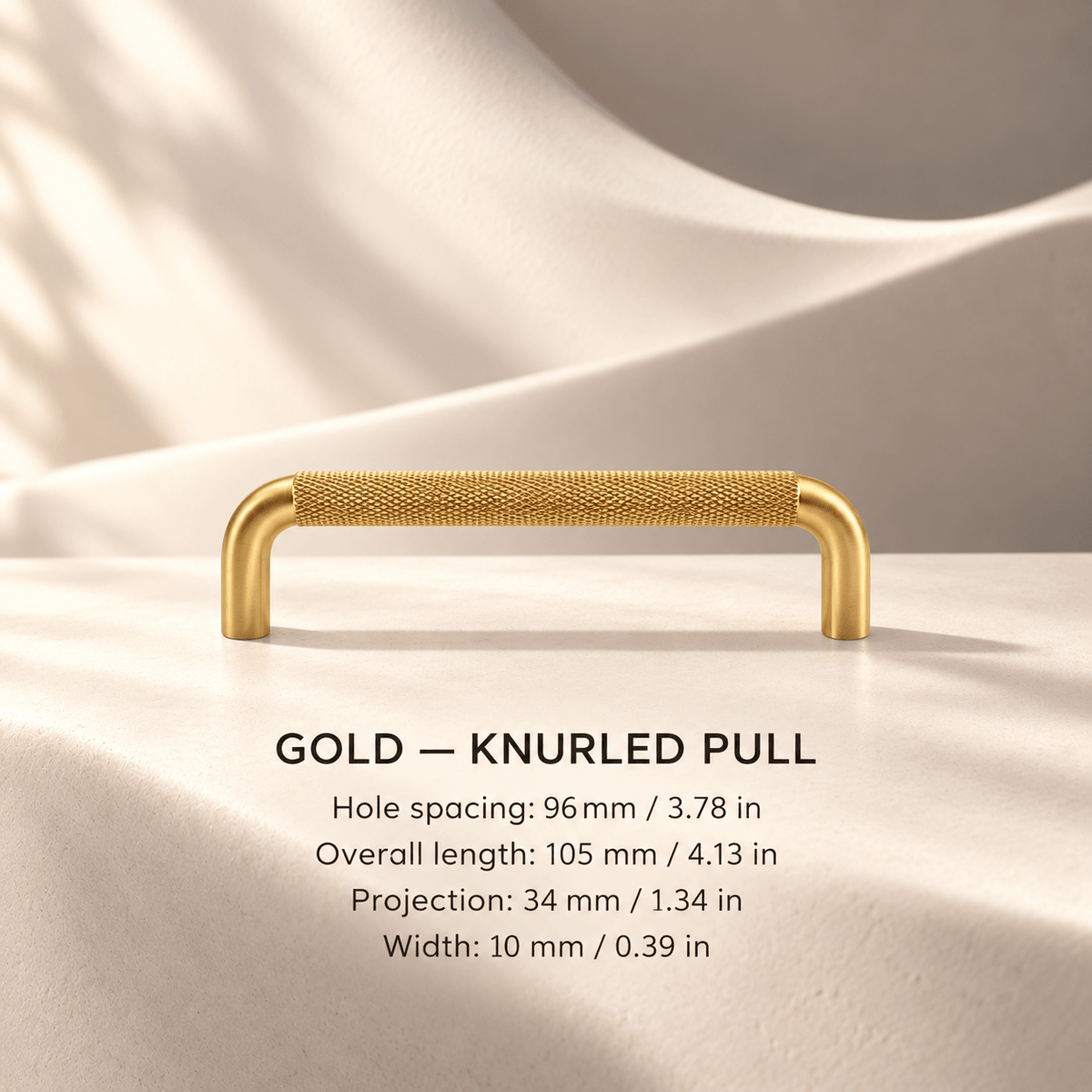 Gold knurled cabinet pull in ivory studio. Hole spacing: 96 mm / 3.78 in; Overall length: 105 mm / 4.13 in; Projection: 34 mm / 1.34 in; Width: 10 mm / 0.39 in