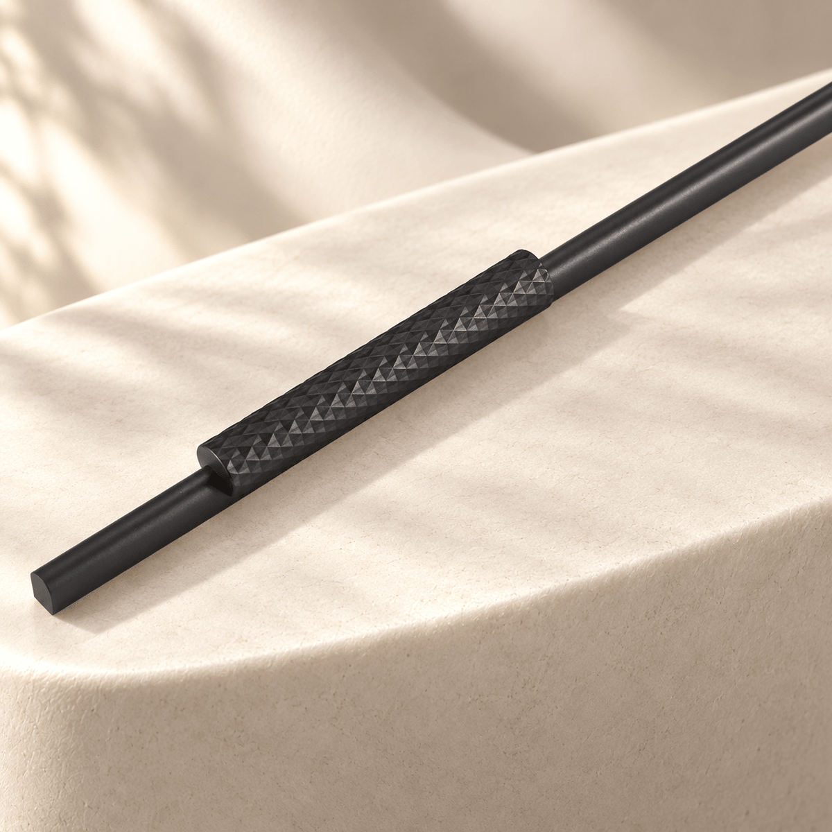 Gray faceted aluminum cabinet handle in a warm ivory stone studio, close-up detail