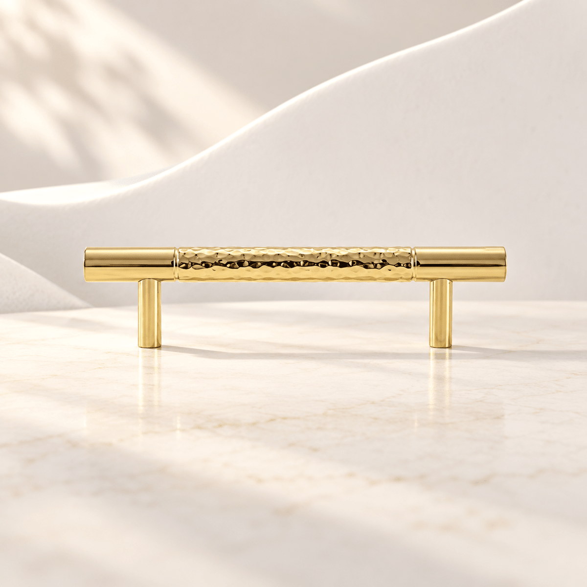 Hammered gold brass cabinet pull with 96 mm (3.78 in) hole spacing on ivory stone