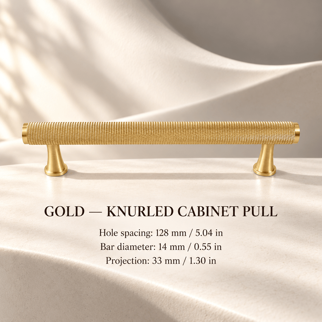 Gold knurled cabinet pull with flared feet in ivory studio. Hole spacing: 128 mm / 5.04 in; Bar diameter: 14 mm / 0.55 in; Projection: 33 mm / 1.30 in