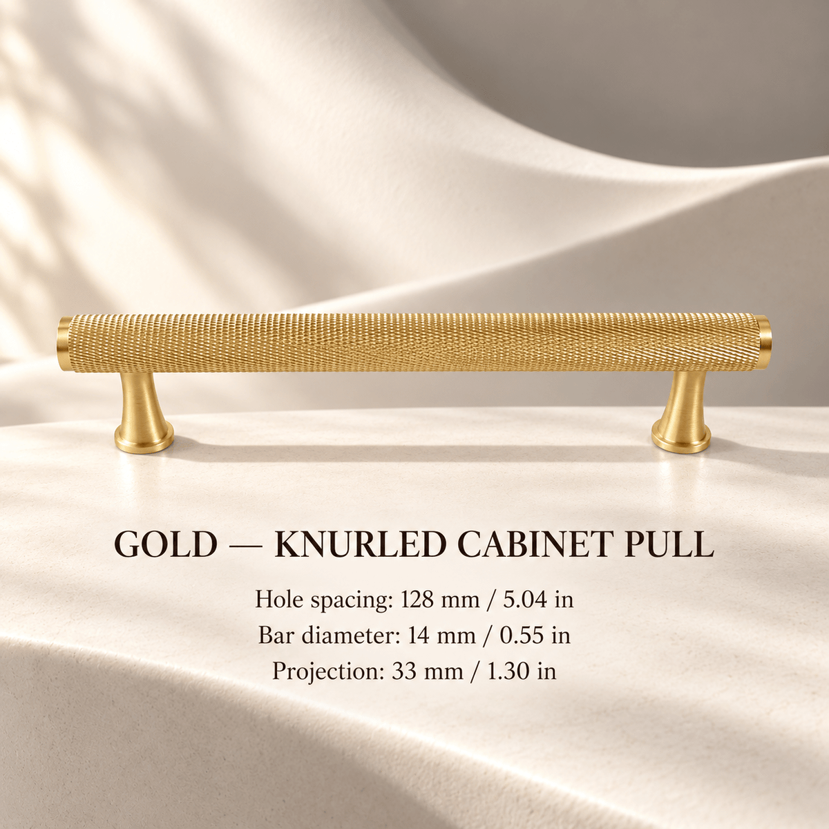 Gold knurled cabinet pull with flared feet in ivory studio. Hole spacing: 128 mm / 5.04 in; Bar diameter: 14 mm / 0.55 in; Projection: 33 mm / 1.30 in