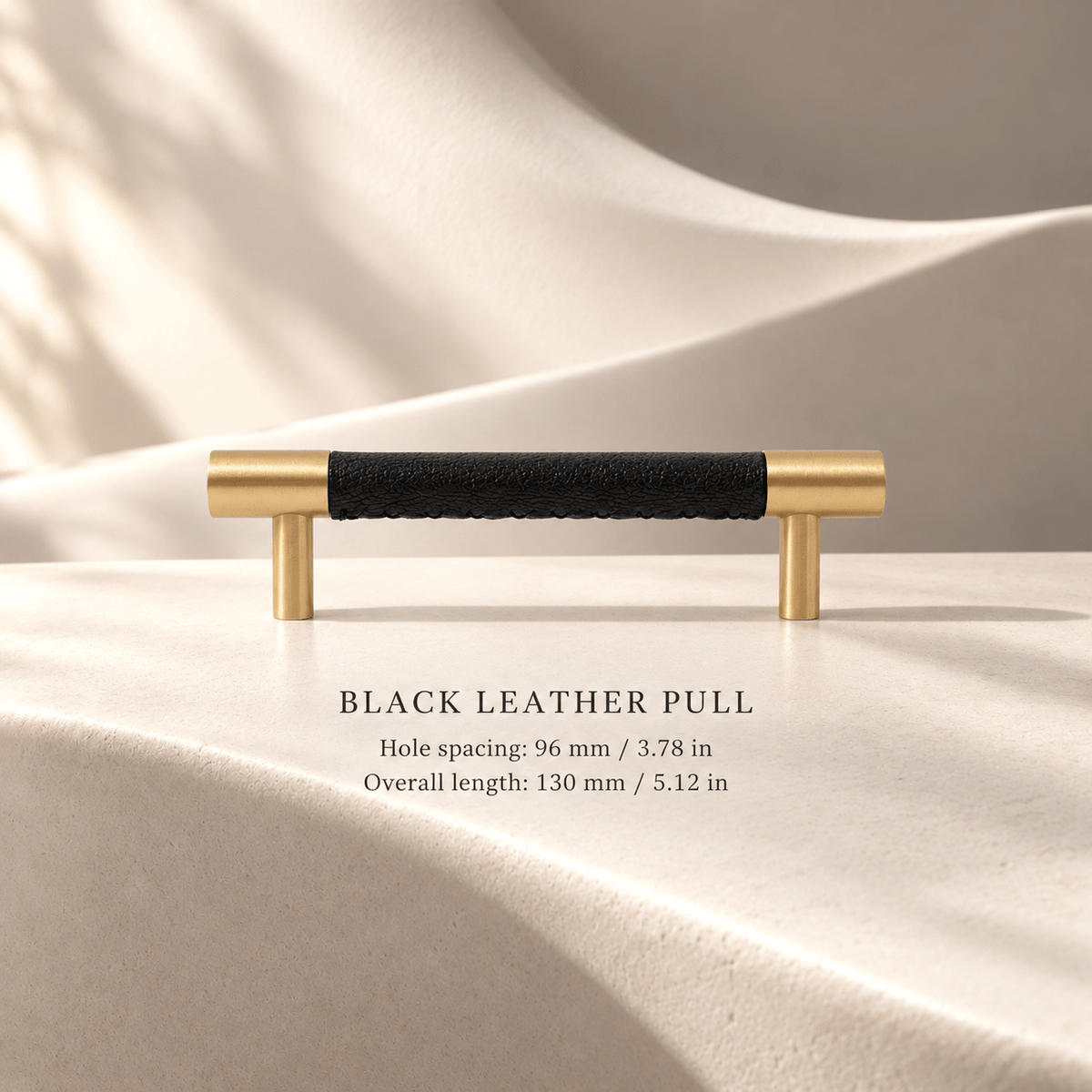 Black leather cabinet pull with gold-tone ends; 96 mm (3.78 in) hole spacing and 130 mm (5.12 in) overall length, ivory studio.