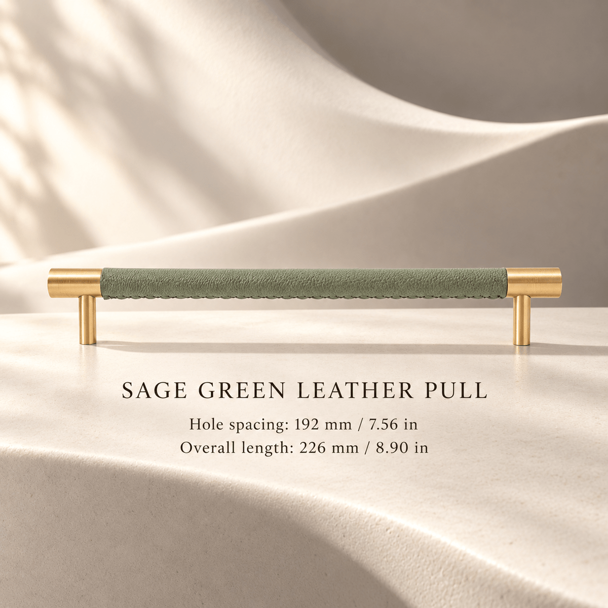 Sage green leather cabinet pull with gold-tone ends; 192 mm (7.56 in) hole spacing and 226 mm (8.90 in) overall length, ivory studio.