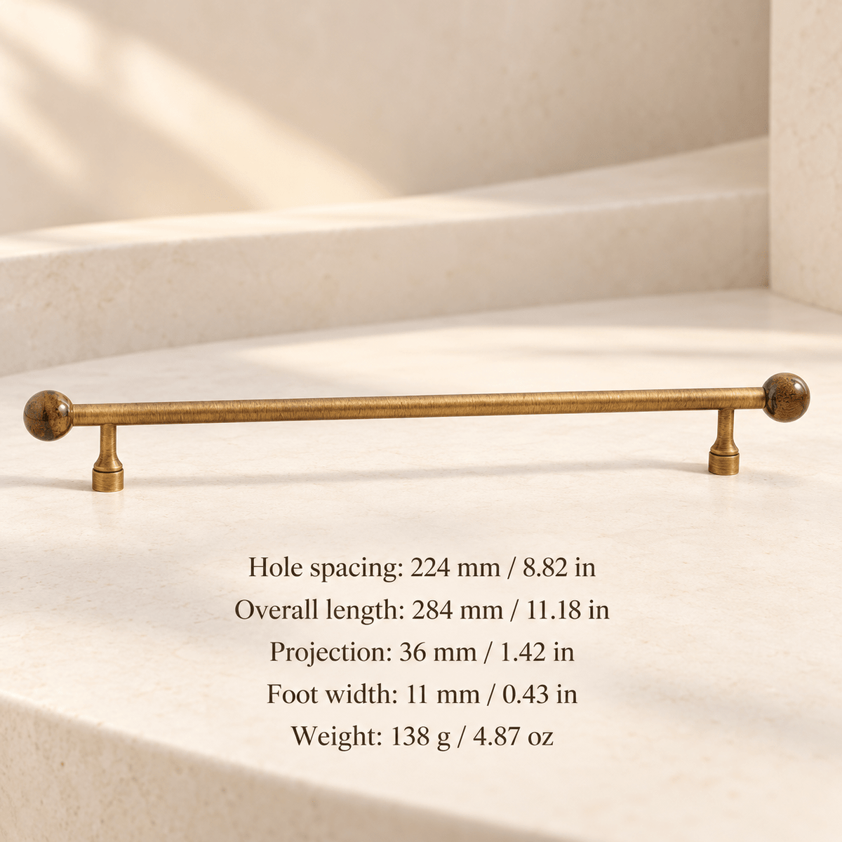 Antique gold cabinet pull with brown patterned ball ends in ivory studio. Hole spacing: 224 mm / 8.82 in; Overall length: 284 mm / 11.18 in; Projection: 36 mm / 1.42 in; Foot width: 11 mm / 0.43 in; Weight: 138 g / 4.87 oz