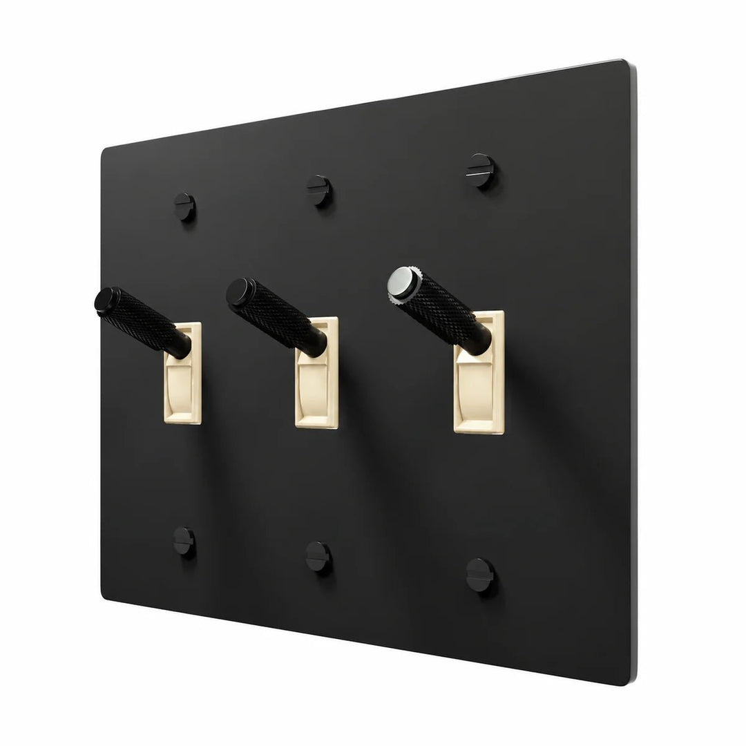 PlatePrestige Brass Toggle Switch 3-Gang in All‑Black with ivory toggle frames, angled view