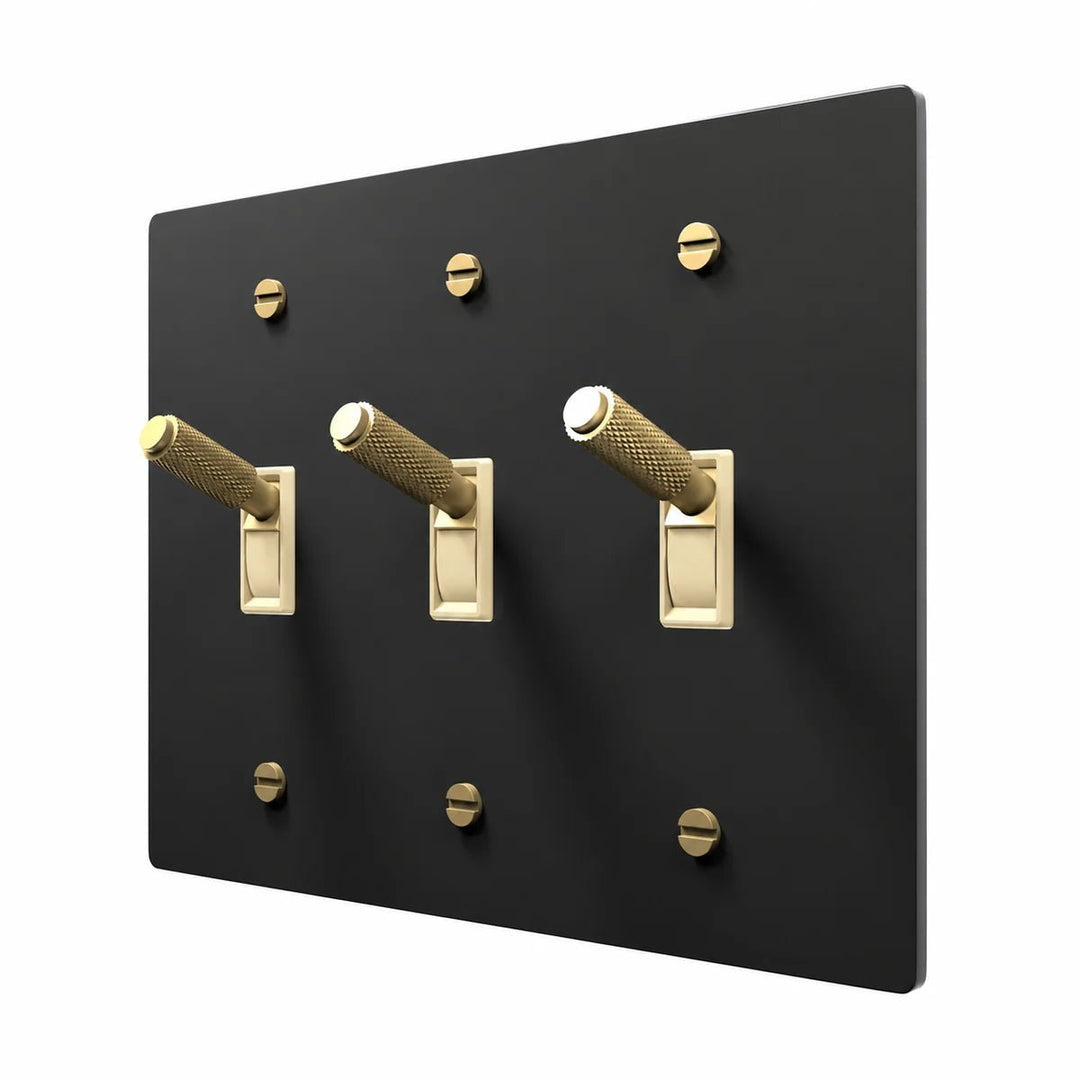 PlatePrestige Brass Toggle Switch 3-Gang in Black / Brass with ivory toggle frames, angled view