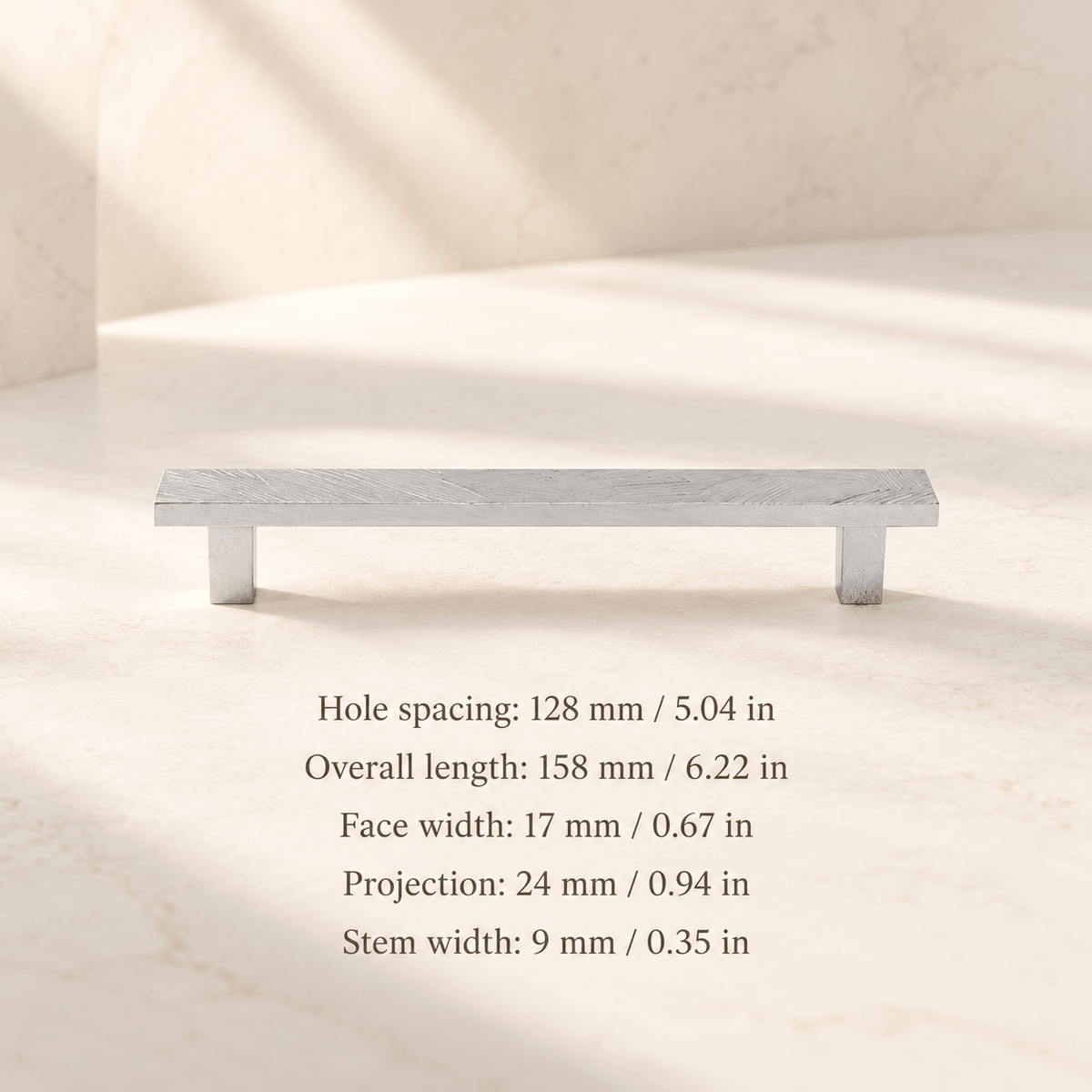 Chrome textured flat cabinet pull in ivory studio. Hole spacing: 128 mm / 5.04 in; Overall length: 158 mm / 6.22 in; Face width: 17 mm / 0.67 in; Projection: 24 mm / 0.94 in; Stem width: 9 mm / 0.35 in